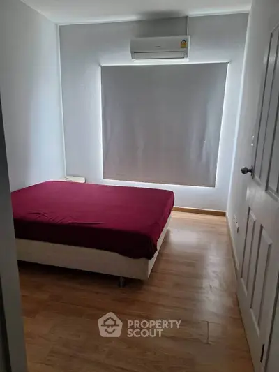 Cozy bedroom with wooden flooring and air conditioning, featuring a minimalist design.