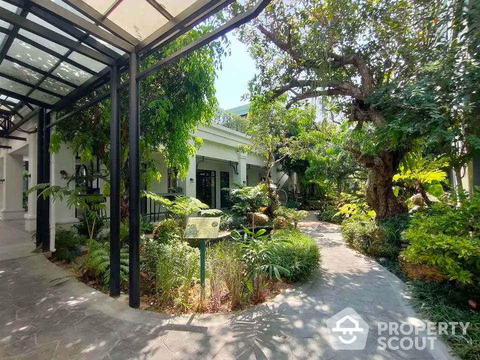 Lush garden entrance with mature trees and pathway leading to a charming house