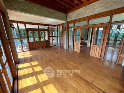 Spacious wooden-floored room with large windows and natural light, perfect for a serene living space.