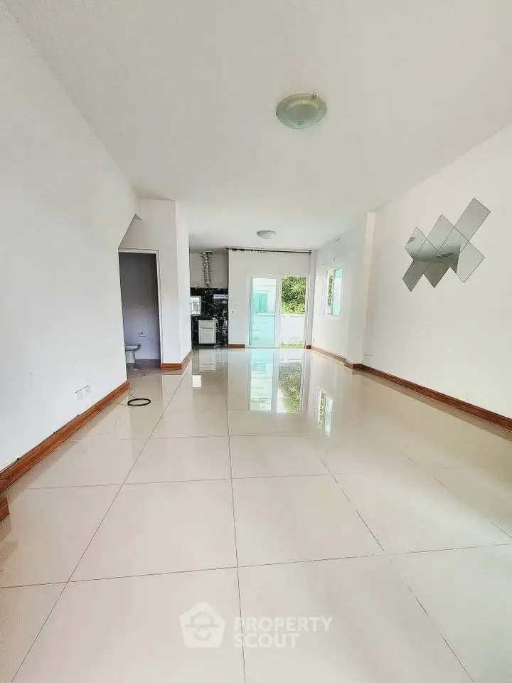 Spacious open-plan living room with glossy tiled floors and modern lighting, leading to a bright kitchen area.