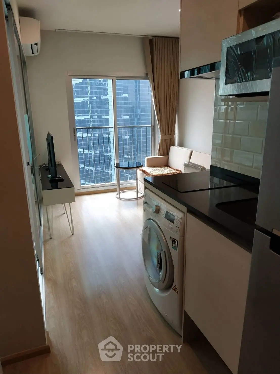 Modern apartment with sleek kitchen and washing machine, featuring a cozy living area and city view.
