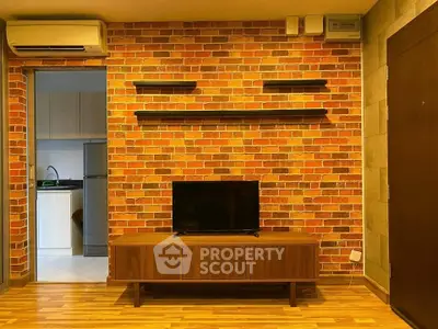 Stylish living room with exposed brick wall and modern TV stand, adjacent to a sleek kitchen.