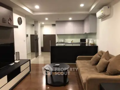 Modern living room with open kitchen, featuring sleek furniture and ambient lighting.