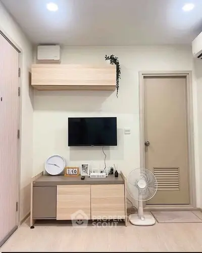 Modern living room with minimalist decor, featuring a wall-mounted TV, sleek wooden furniture, and a standing fan.