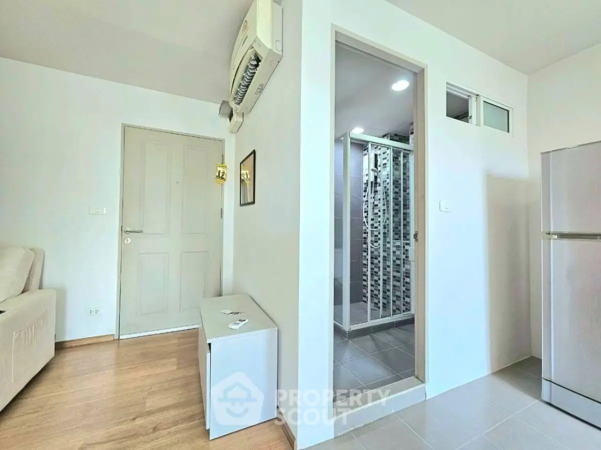 Modern apartment interior with air conditioning, wooden flooring, and a compact kitchen area.
