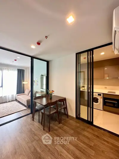 Modern apartment interior with open layout, featuring a cozy living area and sleek kitchen with washing machine.