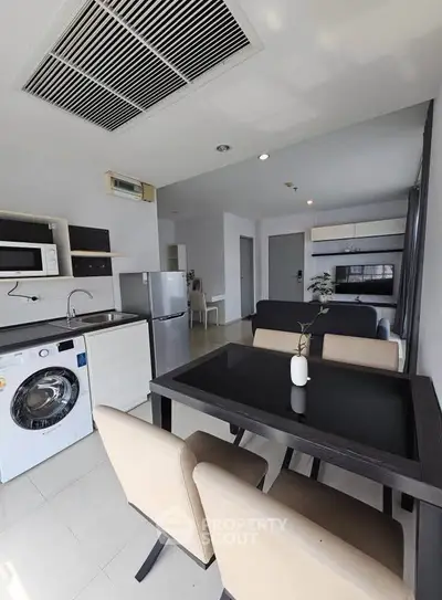 Modern open-layout kitchen and dining area with washing machine and fridge in a bright apartment.