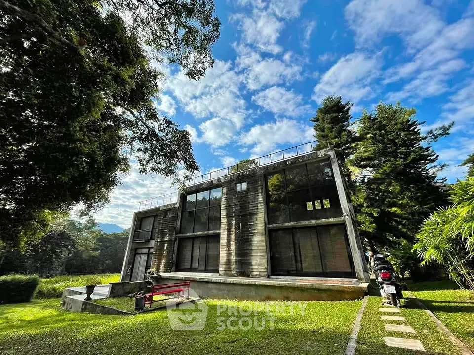 Modern architectural home with large windows surrounded by lush greenery and clear blue sky.