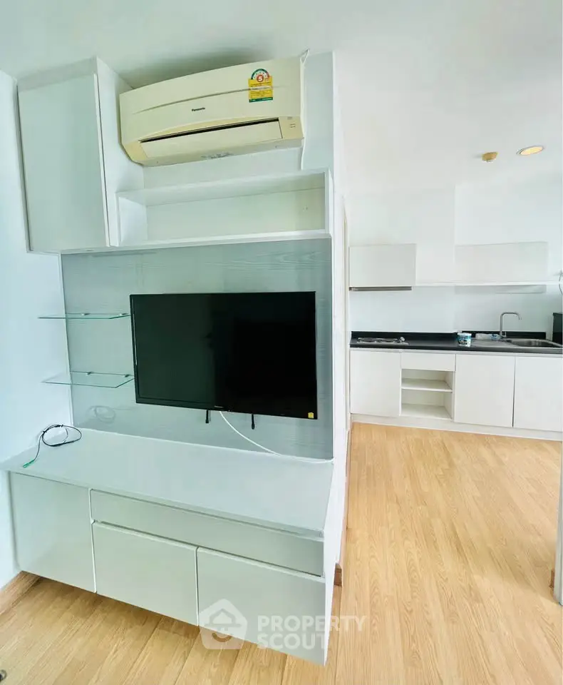 Modern apartment interior with sleek kitchen and wall-mounted TV, featuring wooden flooring and air conditioning.