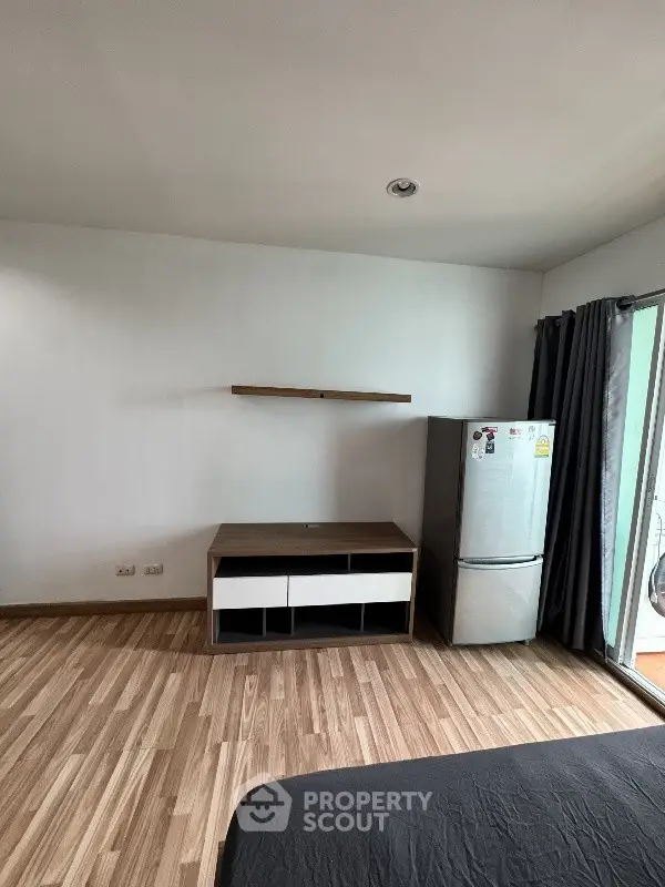 Modern apartment interior with wooden flooring, fridge, and minimalist furniture.