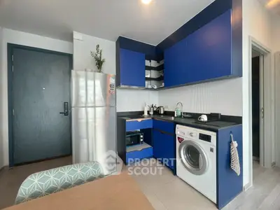 Modern kitchen with blue cabinets, stainless steel fridge, and washing machine in a compact layout.