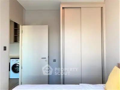 Modern bedroom with built-in wardrobe and view of washing machine in adjacent room.