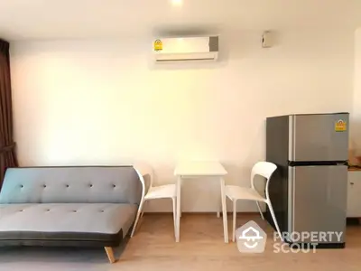 Modern living room with sleek sofa, dining set, and refrigerator under air conditioning.