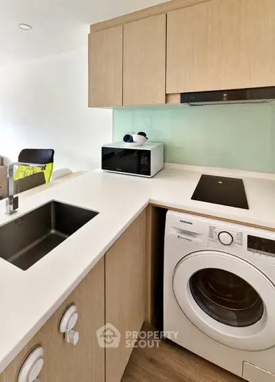 Modern kitchen with sleek appliances and stylish cabinetry, featuring a washing machine and microwave.