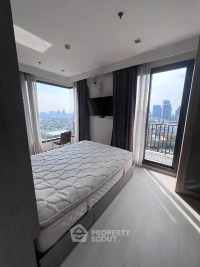 Modern bedroom with city view and balcony access in high-rise apartment.