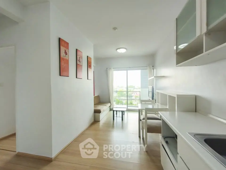 Modern living room with open kitchen and balcony view, featuring sleek design and natural light.