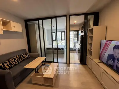 Modern living room with sliding glass doors leading to a bedroom, featuring stylish furniture and a TV.