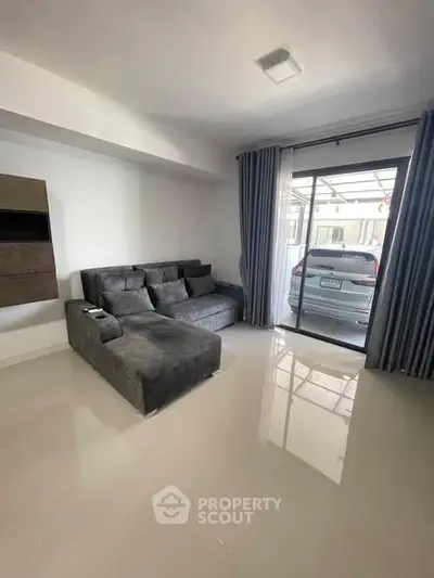 Modern living room with sleek gray sofa and large window overlooking parked car.