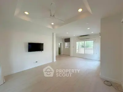 Spacious modern living room with ceiling fan and wall-mounted TV, featuring large windows for natural light.