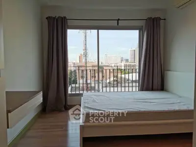 Spacious bedroom with large window offering city view, featuring wooden flooring and modern decor.