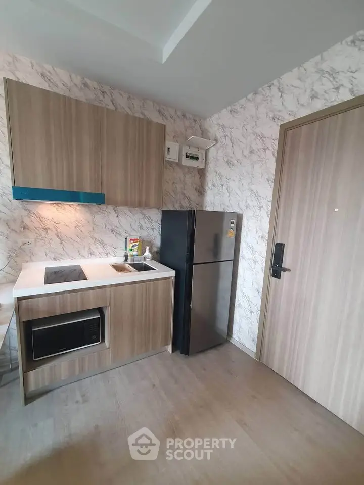 Modern compact kitchen with sleek cabinetry and stainless steel fridge in stylish apartment.