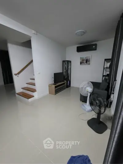 Modern living room with sleek staircase and minimalist decor, featuring air conditioning and stylish furniture.
