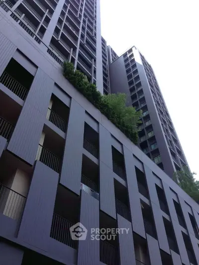 Modern high-rise building exterior with sleek design and lush greenery on upper floors.