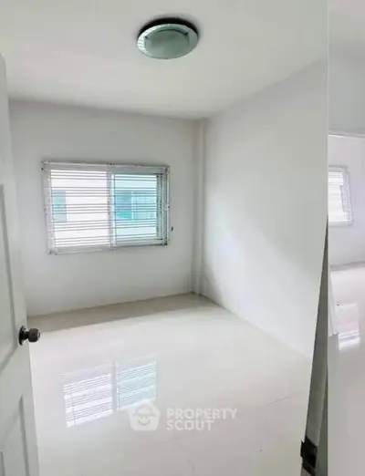 Bright empty room with white walls and large window, perfect for customization.