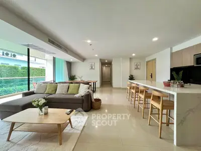 Spacious modern living room with open kitchen and large windows overlooking greenery.