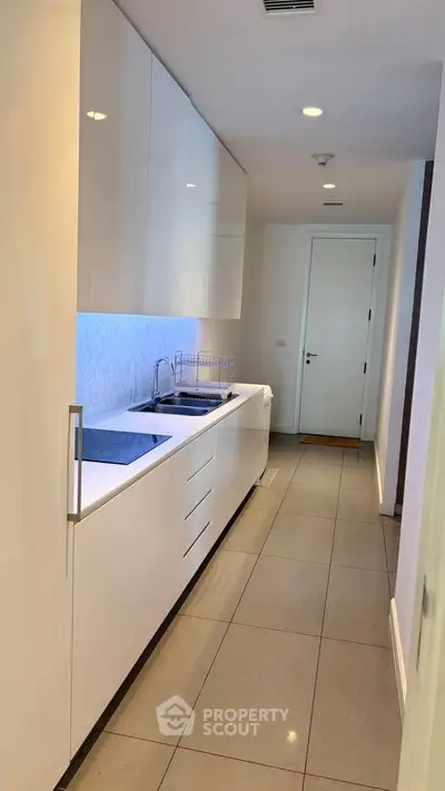 Sleek modern kitchen with glossy cabinets and integrated appliances in a narrow layout.