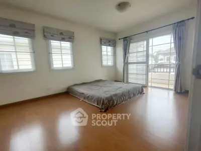 Spacious bedroom with large windows and balcony access, featuring minimalist decor and abundant natural light.