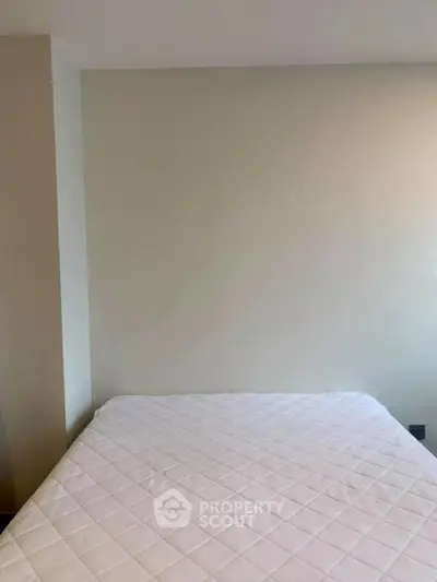 Minimalist bedroom with a neatly made bed and plain walls, perfect for a cozy retreat.