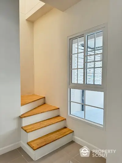 Modern staircase with wooden steps and large window in bright interior