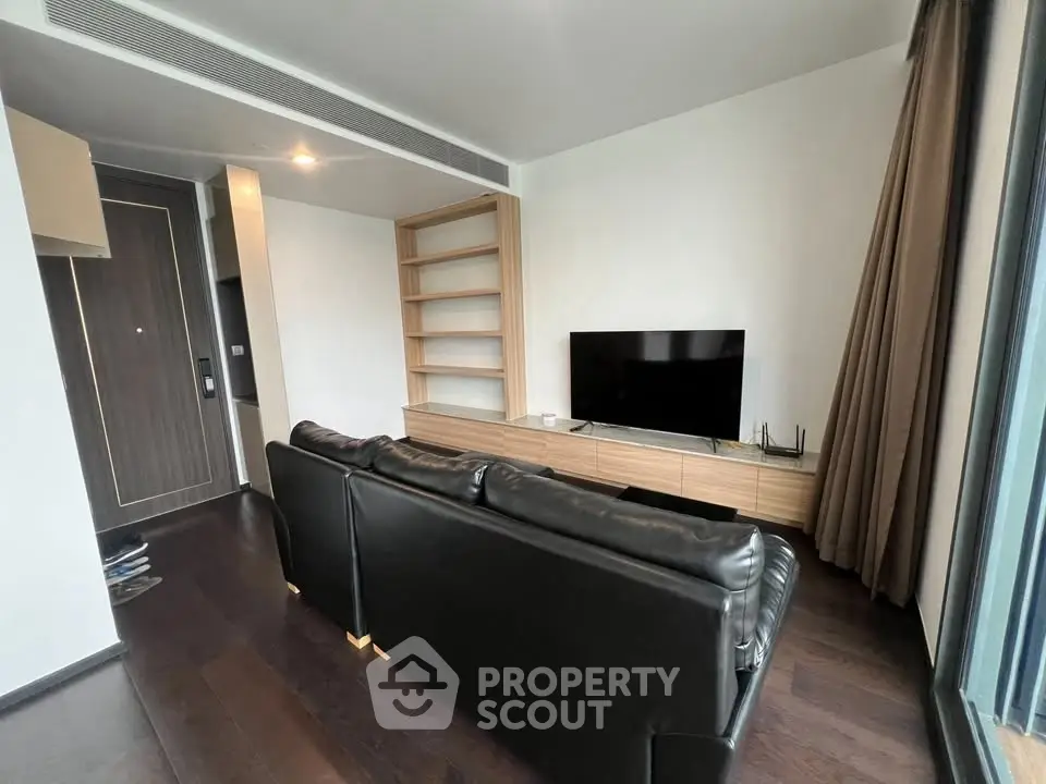 Modern living room with sleek black leather sofa and large TV, featuring built-in wooden shelving.