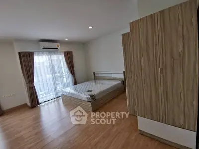 Spacious bedroom with wooden flooring and large window for natural light.