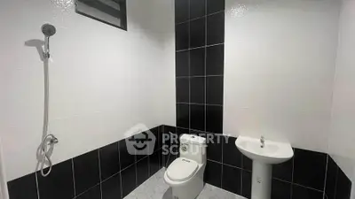 Modern bathroom with sleek black and white tiles, featuring a shower, toilet, and pedestal sink.