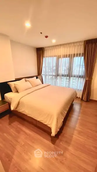 Spacious bedroom with large windows and elegant curtains in modern apartment.
