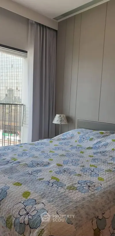 Cozy bedroom with floral bedding and city view from window, perfect for urban living.