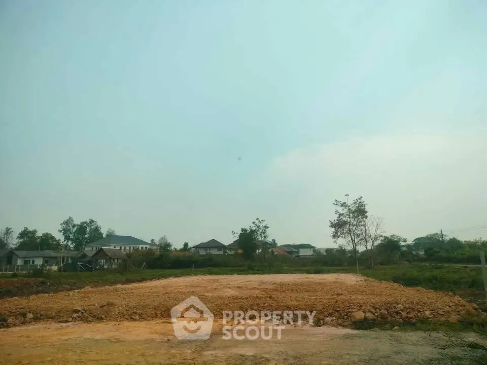 Expansive land plot with potential for residential development, surrounded by greenery and nearby homes.