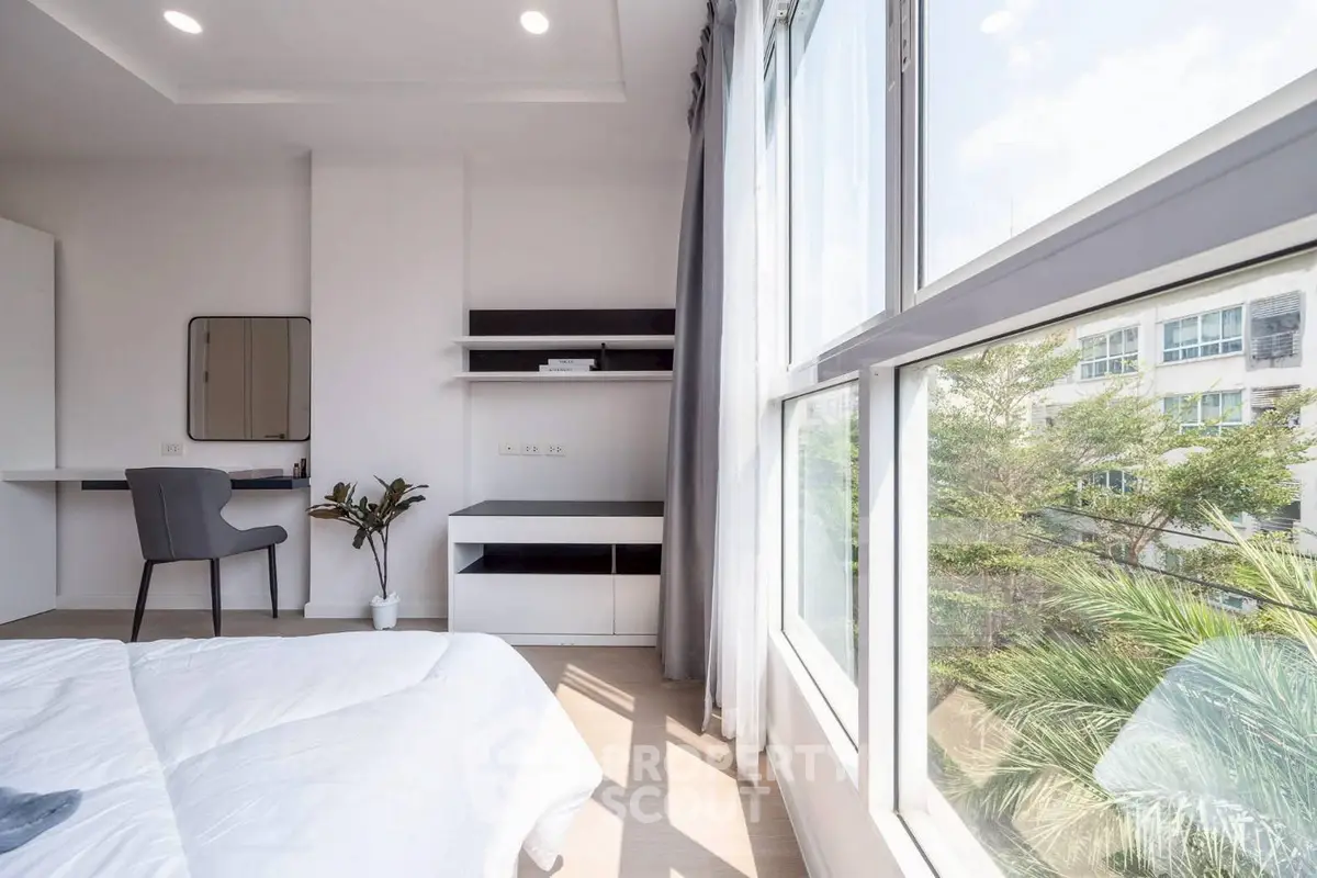 Bright bedroom with large windows and modern decor, offering a serene view of greenery outside.