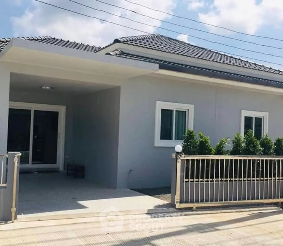 Modern single-story house with sleek design and gated entrance under a clear blue sky.