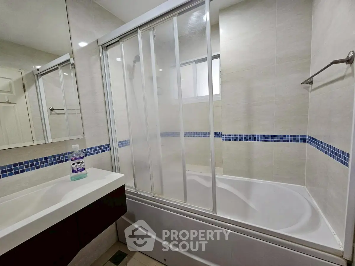 Modern bathroom with bathtub and sliding glass doors, featuring sleek design and contemporary fixtures.