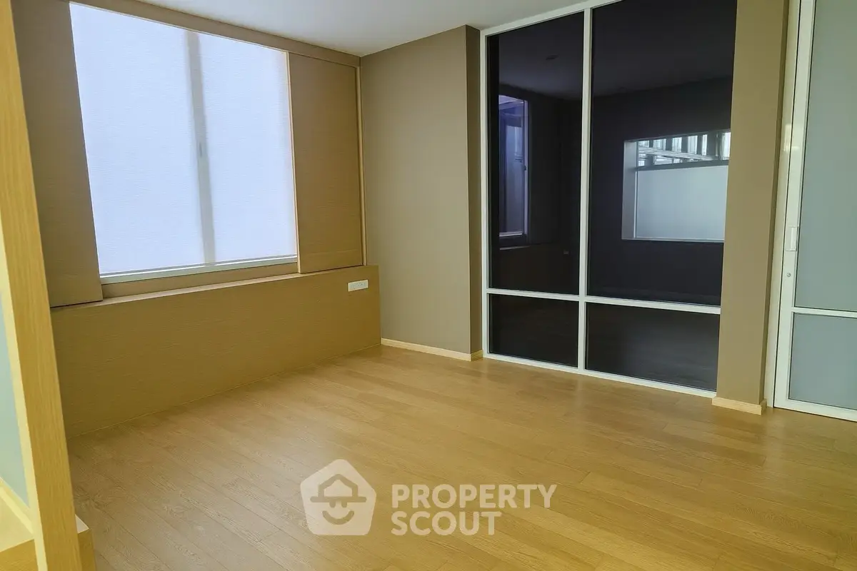 Spacious empty room with wooden flooring and large window, perfect for customization.