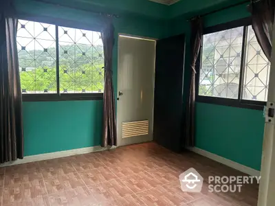 Spacious room with large windows, natural light, and a serene view, featuring elegant dark curtains and a vibrant green wall, perfect for a cozy living space.