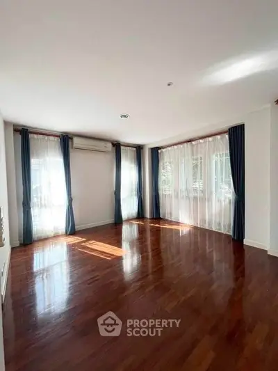 Spacious sunlit living room with hardwood floors and large windows in modern apartment.