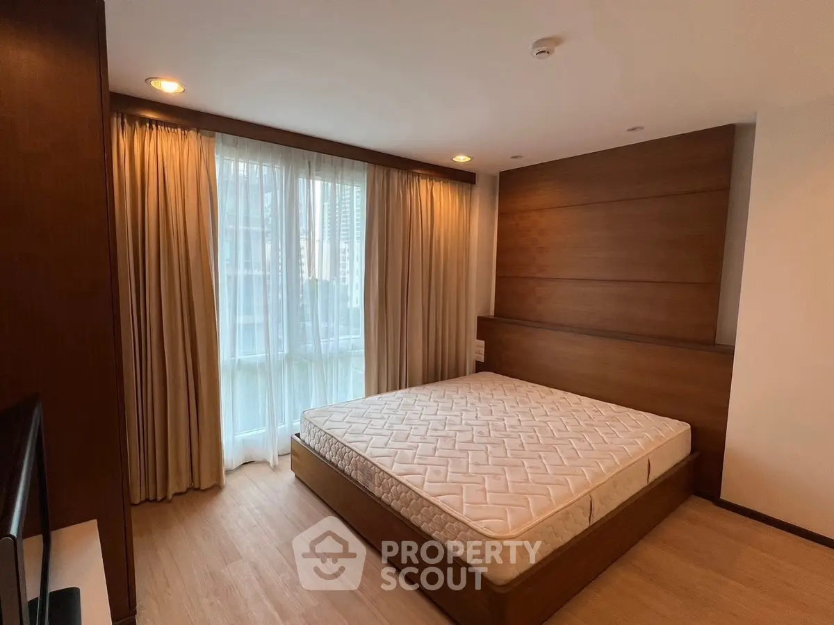 Modern bedroom with wooden accents and large window in urban apartment.