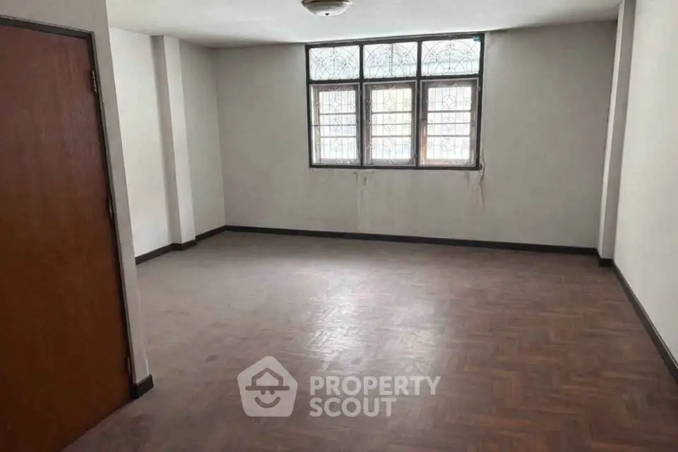 Spacious empty room with parquet flooring and large windows, ideal for customization.