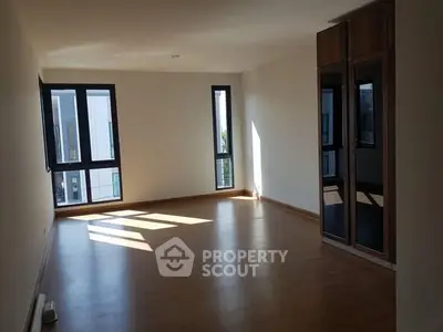 Spacious empty room with wooden flooring and large windows for natural light.