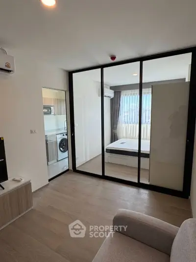 Modern apartment interior with glass partition, cozy living area, and compact kitchen.
