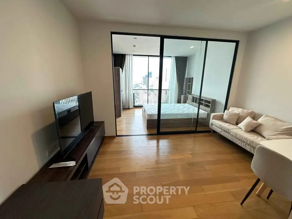 Modern apartment with open layout featuring a cozy living room and bedroom separated by glass doors.